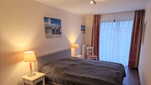 Een hotelkamer met een groot bed, twee nachtkastjes, een stoel en een raam met gordijnen.