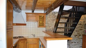 A kitchen with wooden cabinets, a stone wall, and a wooden staircase. - Amazing home in Plozevet with kitchen (Plozevet)