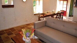 A living room with a sofa, a dining table with chairs, a vase of flowers, and a wall-mounted light fixture. - Amazing home in Plozevet with kitchen (Plozevet)