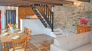 A dining area with a wooden table set for four, a staircase leading to an upper level, and a stone wall. - Amazing home in Plozevet with kitchen (Plozevet)