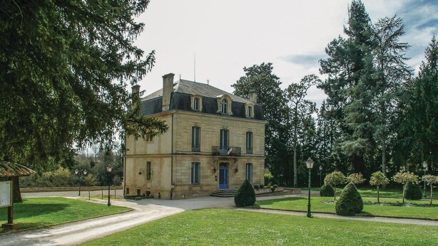 Ein zweistöckiges Gebäude mit einer symmetrischen Fassade, einem zentralen Eingang mit Treppe und einer Flagge im zweiten Stock.