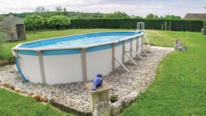 Ein rechteckiger Pool, der oberirdisch installiert ist, mit einer Leiter an einer Seite, umgeben von einem Kiesbett und einem kleinen Gartenbereich mit einer Vogelstatue.