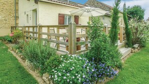 Ein rustikales Steinhaus mit einer Holzterrasse und einem Garten mit Blumen und Sträuchern.