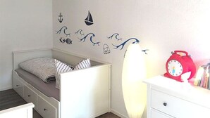 Ein Kinderzimmer mit Etagenbett, einer kleinen Bank, einem Schminktisch und einer Wand mit maritimen Aufklebern.