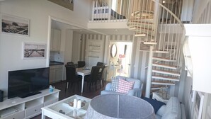 Ein geräumiges Wohnzimmer mit Fernseher, Essbereich und einer Treppe, die in eine obere Etage führt.