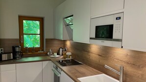 Eine moderne Küche mit weißen Schränken, einer Holzarbeitsplatte, einem eingebauten Backofen, einer Mikrowelle und einem Fenster mit Blick ins Grüne.