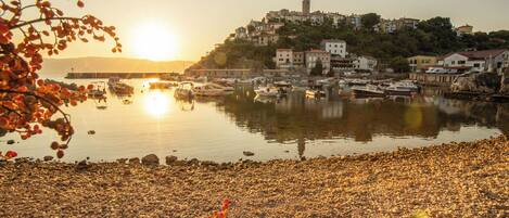 A coastal town with boats docked at a harbor, buildings on a hillside, and a clear sky.