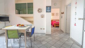 A dining area with a table and chairs, a television, and a kitchen area with cabinets and a sink.