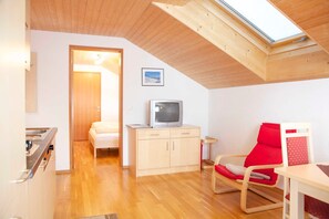 A compact room with a wooden ceiling, a television on a cabinet, a red chair, and a bed in the background.
