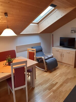 A cozy loft-style room with a dining table, chairs, a sofa, a recliner, a TV, and a skylight.