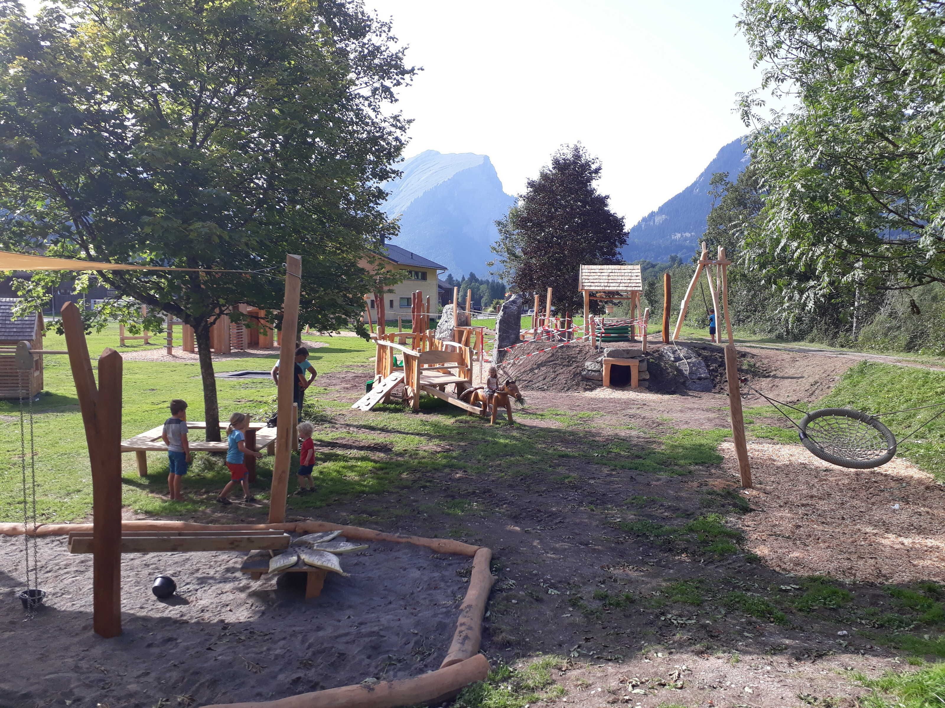 Un parc infantil amb cadira de balanceig, elements per pujar i un espai amb sorra.