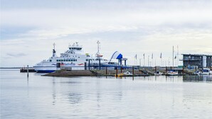 Um ferry atracado em um cais, com um pequeno edifício próximo.