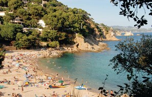 Ein Strand mit badenden und sonnenden Menschen, umgeben von Häusern und Bäumen.