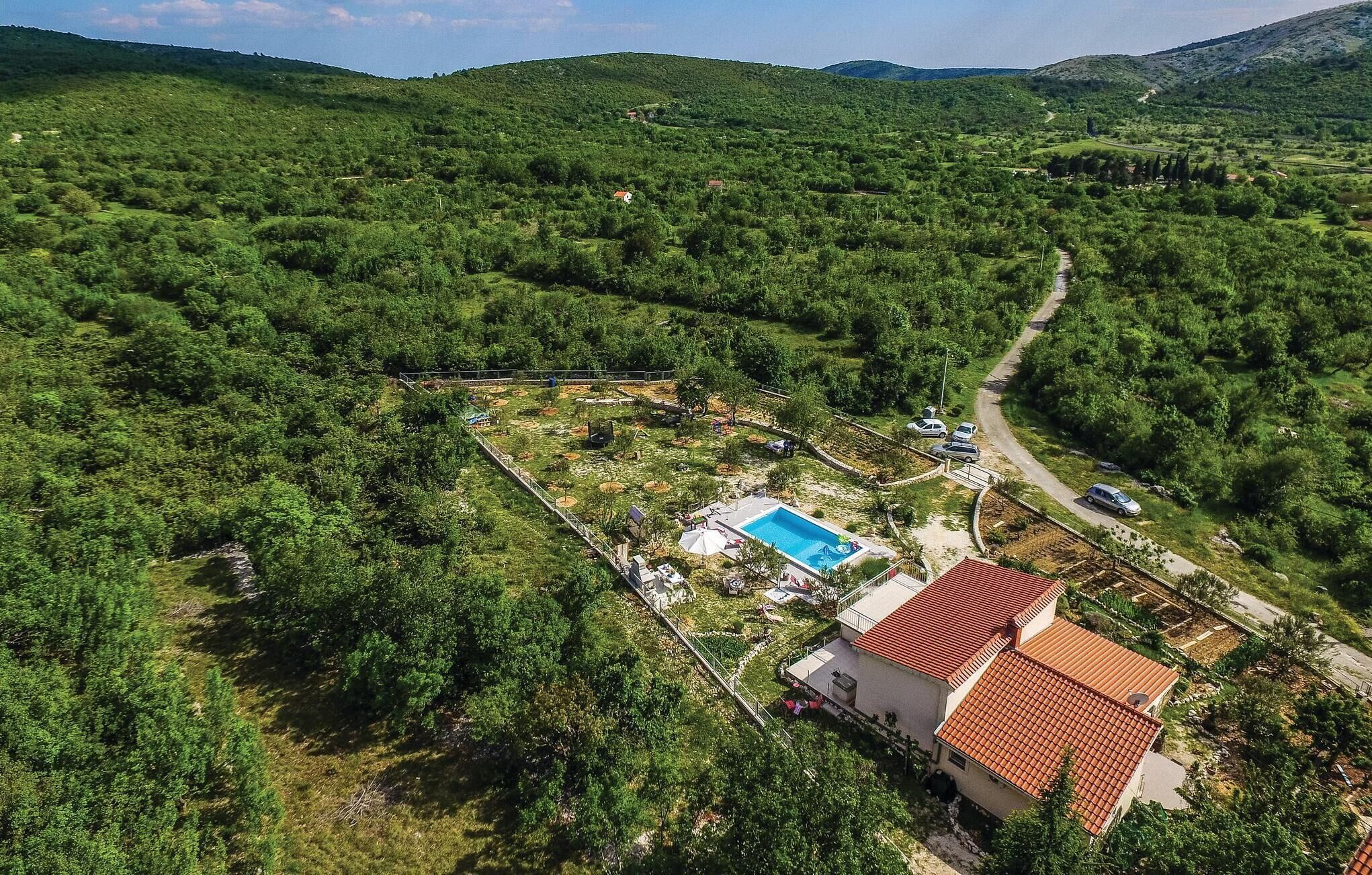 Ett bostadsområde med en swimmingpool, ett hus med ett rött tegeltak och en väg som slingrar sig genom kullarna.