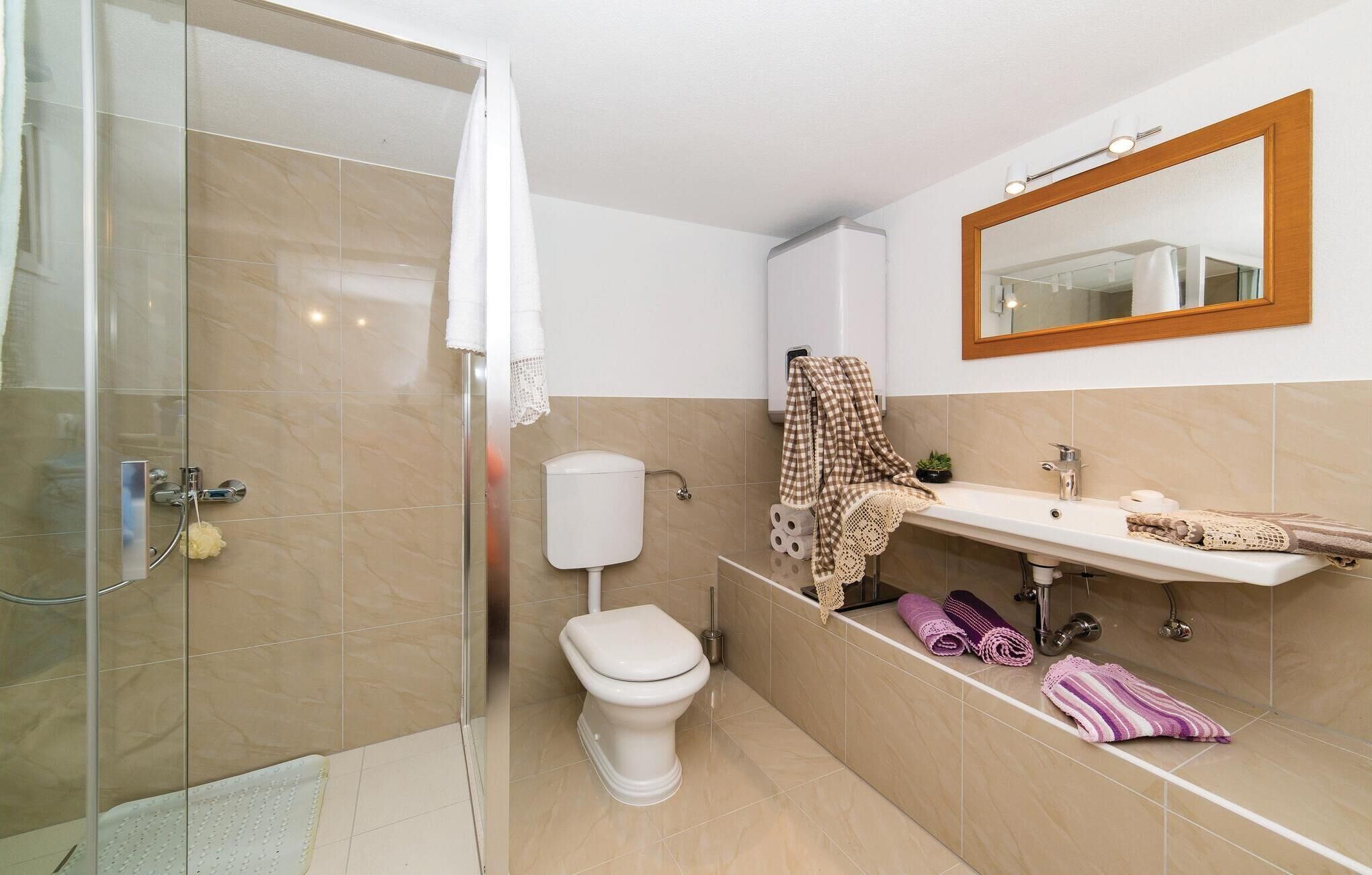 A bathroom with a glass shower enclosure, a toilet, a sink with a mirror, and towels.