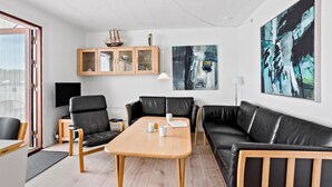 A modern living room with a wooden coffee table, black leather sofas, a wooden cabinet with glass doors, and abstract paintings on the walls. - 1 bedroom amazing home in Tranekær (Tranekær)