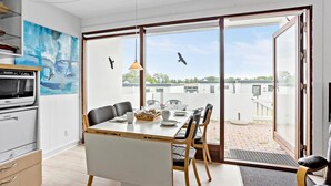 A modern kitchen with a Siemens oven, a dining area with a table and chairs, and a large window with a view of buildings and trees. - 1 bedroom amazing home in Tranekær (Tranekær)