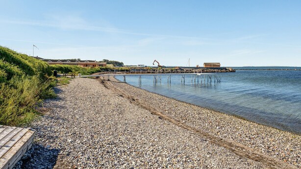 A pebbled beach with a wooden walkway leading to a pier extending into calm waters. - 1 bedroom amazing home in Tranekær (Tranekær)