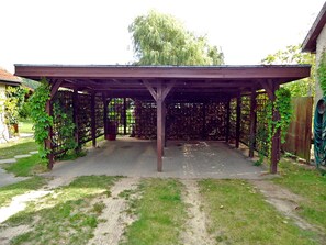Un área de patio techada con una estructura de pérgola, rodeada por una cerca de madera y un jardín.
