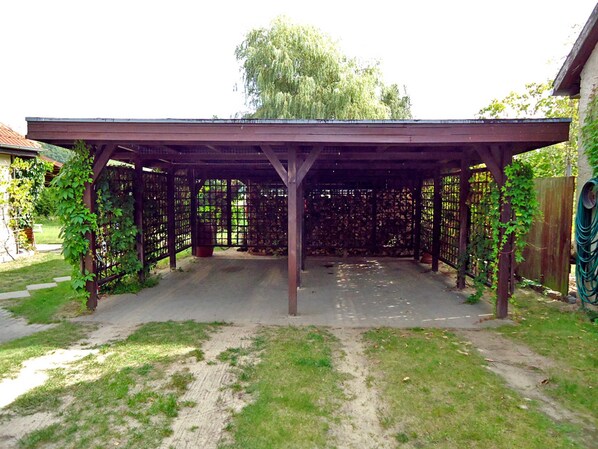 Ein überdachter Patio-Bereich mit einer Pergola, umgeben von einem Holzzaun und einem Garten.