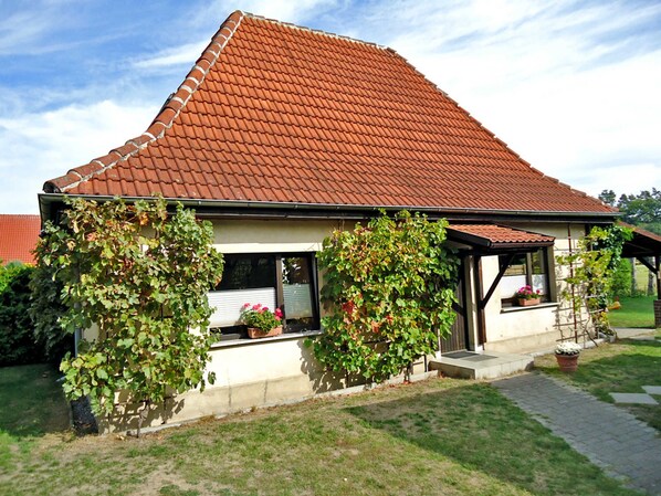 A house with a red-tiled roof, a covered porch, and a garden with potted plants.