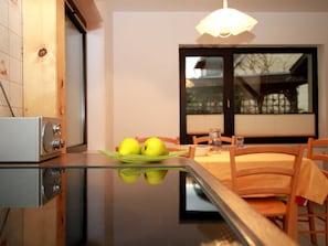 Ett modernt kök med ett glasbord som reflekterar två äpplen på en grön tallrik, träskåp och ett fönster med utsikt över ett hus.