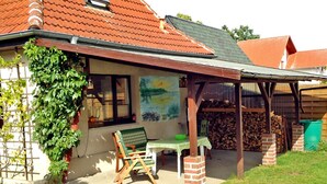 Ein Haus mit überdachter Terrasse, einem grünen Stuhl, einem Tisch und einem Gemälde an der Wand.