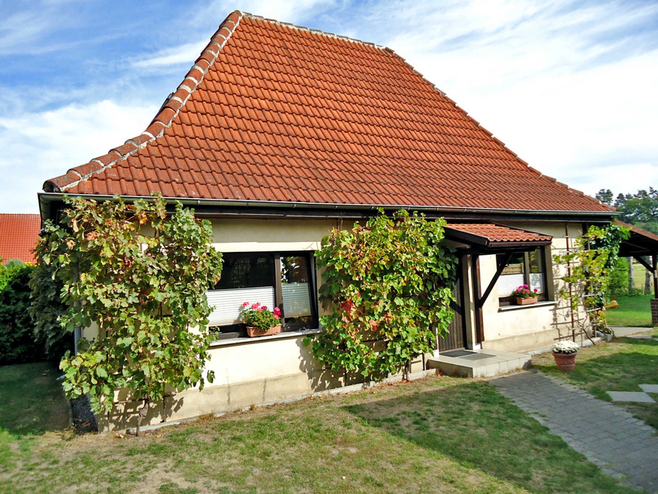 A house with a red-tiled roof, a covered porch, and a garden with potted plants.