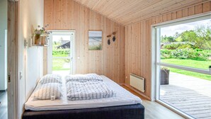 A bedroom with a bed, wooden walls, a view of the outdoors, and a window.