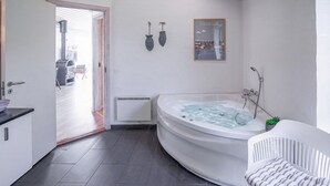 A modern bathroom with a large bathtub, a shower, and a small window.