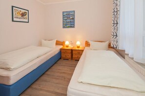 Une chambre avec deux lits simples, des tables de chevet en bois avec des lampes, un tableau encadré et une œuvre d’art bleue accrochée au mur.