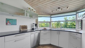 Moderni keittiö, jossa on valkoiset kaapit, sisäänrakennettu uuni, kahvinkeitin ja ikkuna, josta avautuu näkymä vehreään maisemaan.