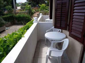Een klein balkon met een witte tafel en twee stoelen, omringd door groen en een stenen muur.