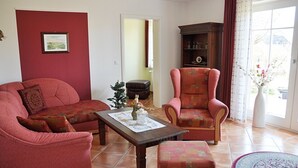 A living room with a red sofa, a matching armchair, a wooden coffee table, and a bookshelf.