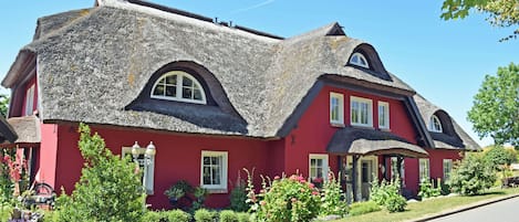 A red house with a thatched roof, a front porch, and a garden.