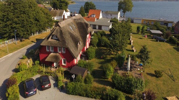 A red house with a thatched roof, a paved driveway, and a body of water in the background.