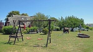 A park with a swing set, a boat, and a thatched-roof building.