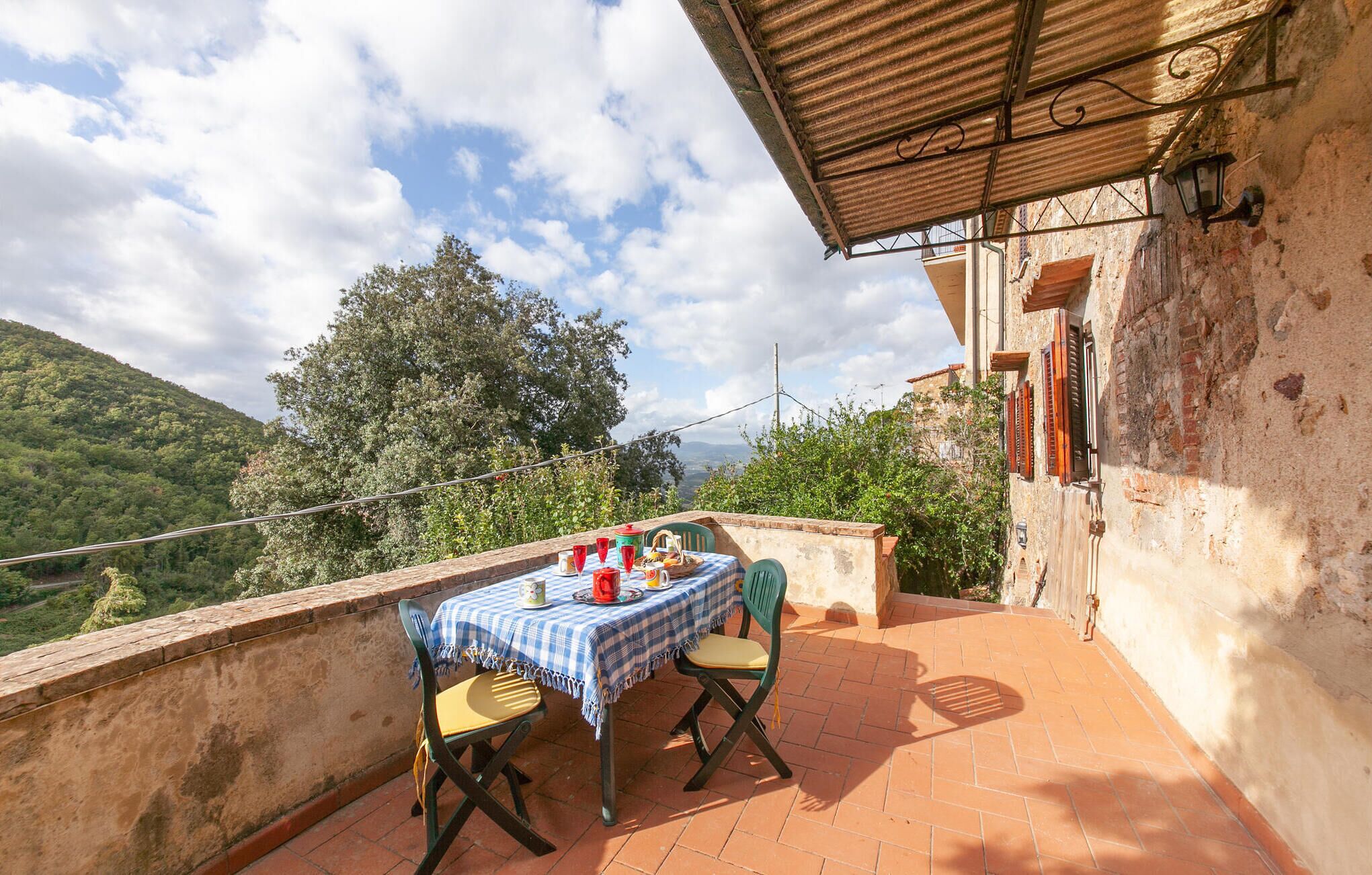 A terrace with a table set for two, overlooking a mountainous landscape.
