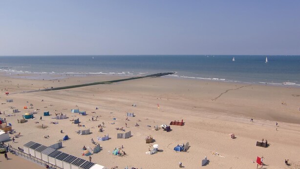 Ein Strand mit Zelten und Liegestühlen, eine Mole, die ins Meer ragt, und ein klarer Himmel.