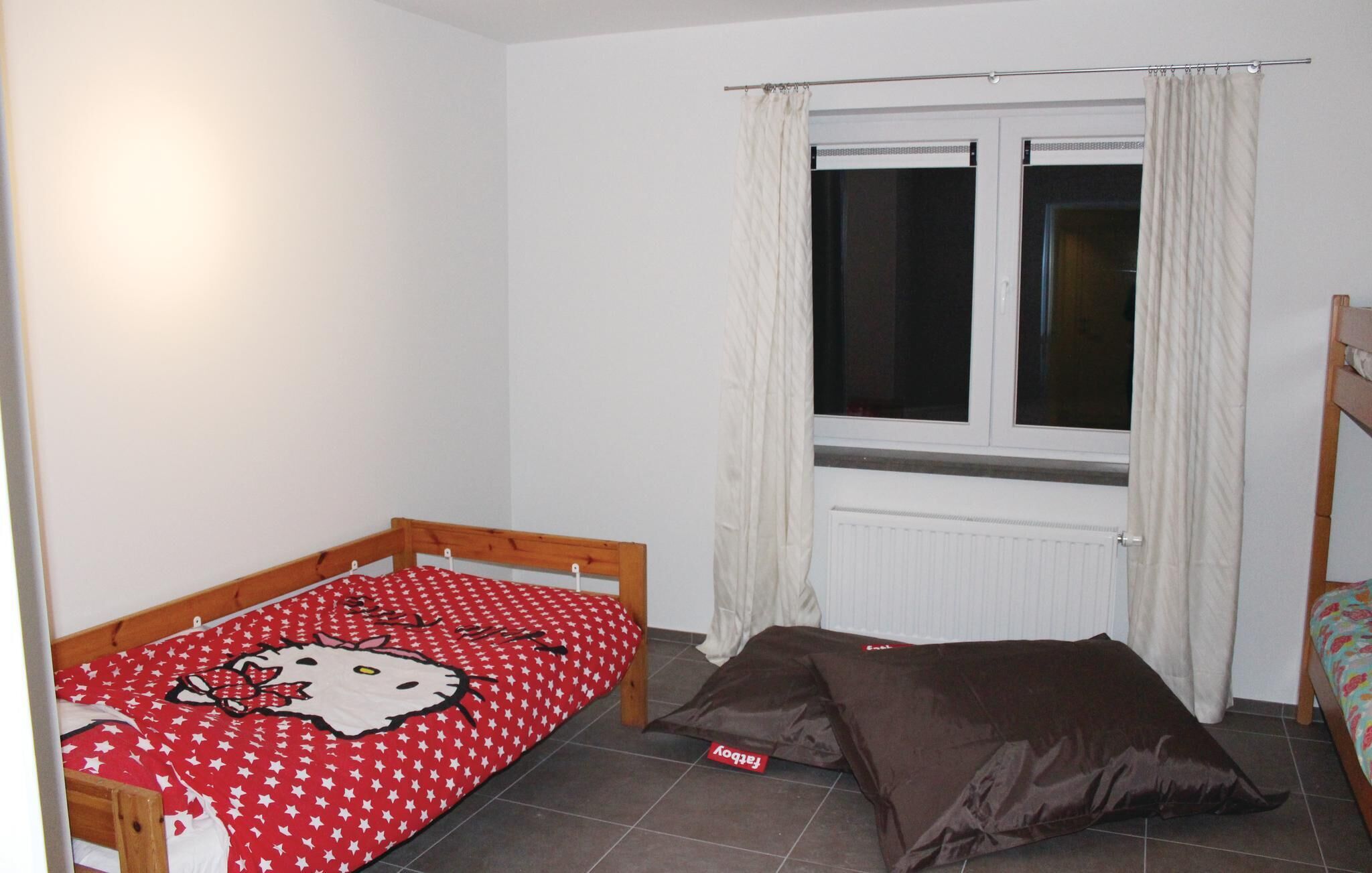 Una habitación pequeña con una cama individual, una ventana con cortinas y un radiador.