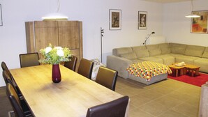 Ein Wohnzimmer mit Esstisch aus Holz, Stühlen, einer Couch und einem farbenfrohen Hocker.