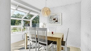A dining area with a wooden table and white chairs, a hanging light fixture, and a white brick wall with a framed picture. - 3 bedroom gorgeous home in Toftlund (Toftlund)