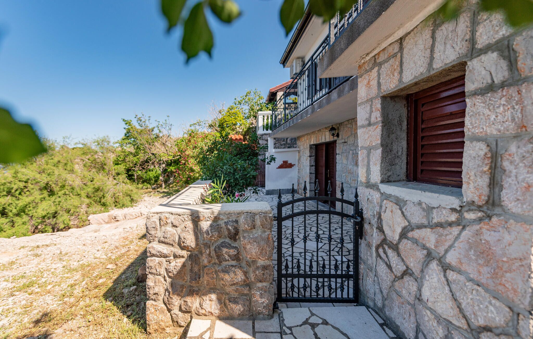 A stone house with a gated entrance, a balcony, and a window with shutters.