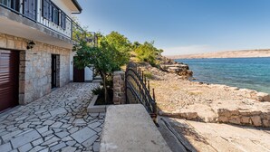 Une propriété située sur la côte, avec une allée d’entrée pavée de pierres, un balcon doté de rampes en métal et une vue sur la mer.