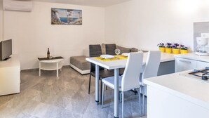 Un salon moderne et bien éclairé, avec une table à manger pour deux personnes, un canapé, une petite table d’appoint et un téléviseur.