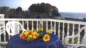 Ein Tisch mit Obst und Blumen auf einem Balkon mit Blick auf das Meer.