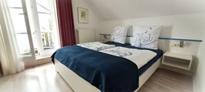A bedroom with a bed, a nightstand, a window with curtains, and a radiator. - 2-space; SÜ 05 - Haus Südstrand (Sierksdorf)