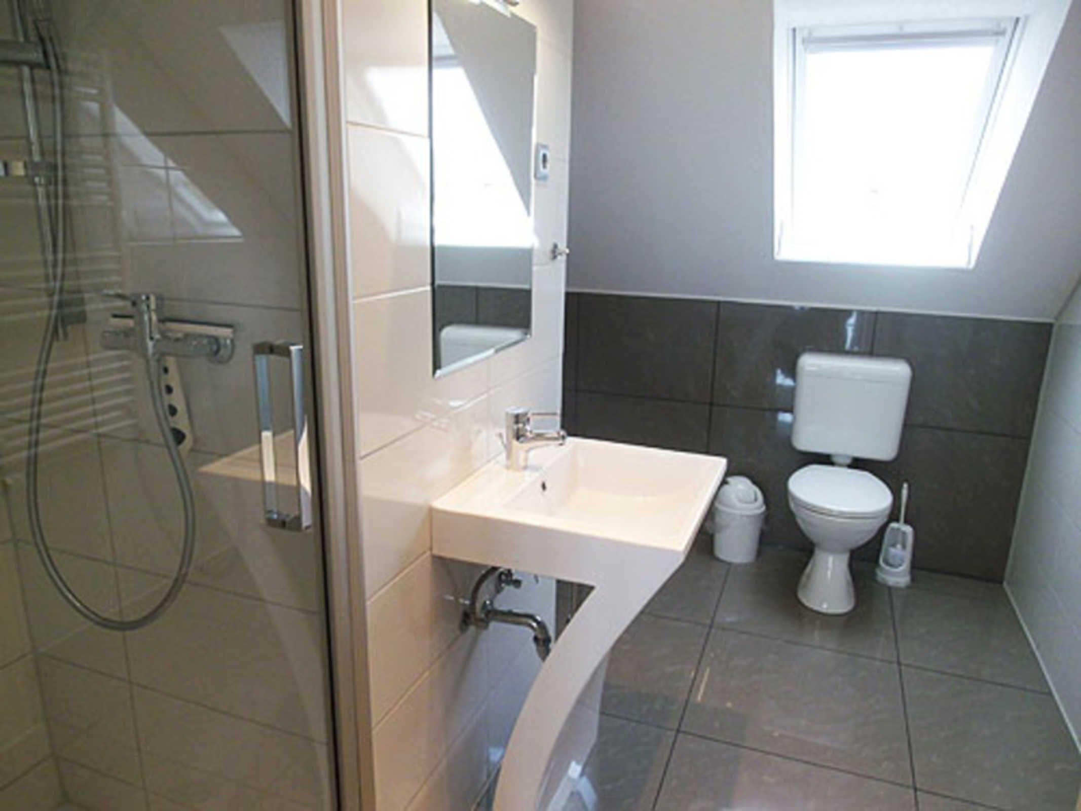 A bathroom with a glass-enclosed shower, a white sink, a mirror, a toilet, and a window.