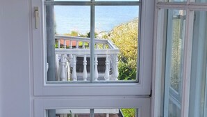 Ein Zimmer mit großem Fenster und Blick auf einen Balkon mit Geländer und Pflanzen.