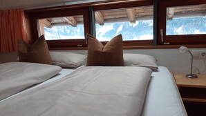 A bedroom with two beds, wooden headboard, a nightstand with a lamp, and a window with a mountain view.